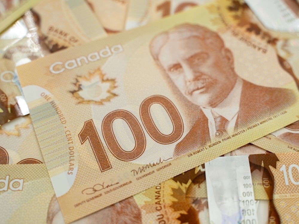 A photo of overlapping $100 bills in Canadian currency. The bills show an image of Robert Borden and are brown in colour.