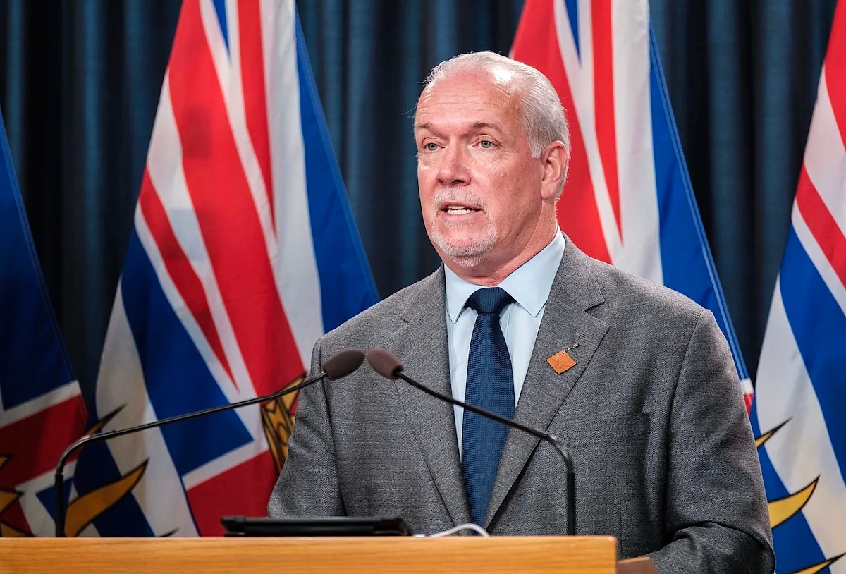John Horgan, a 60-ish man with light skin and thinning grey hair, stands at a lectern.