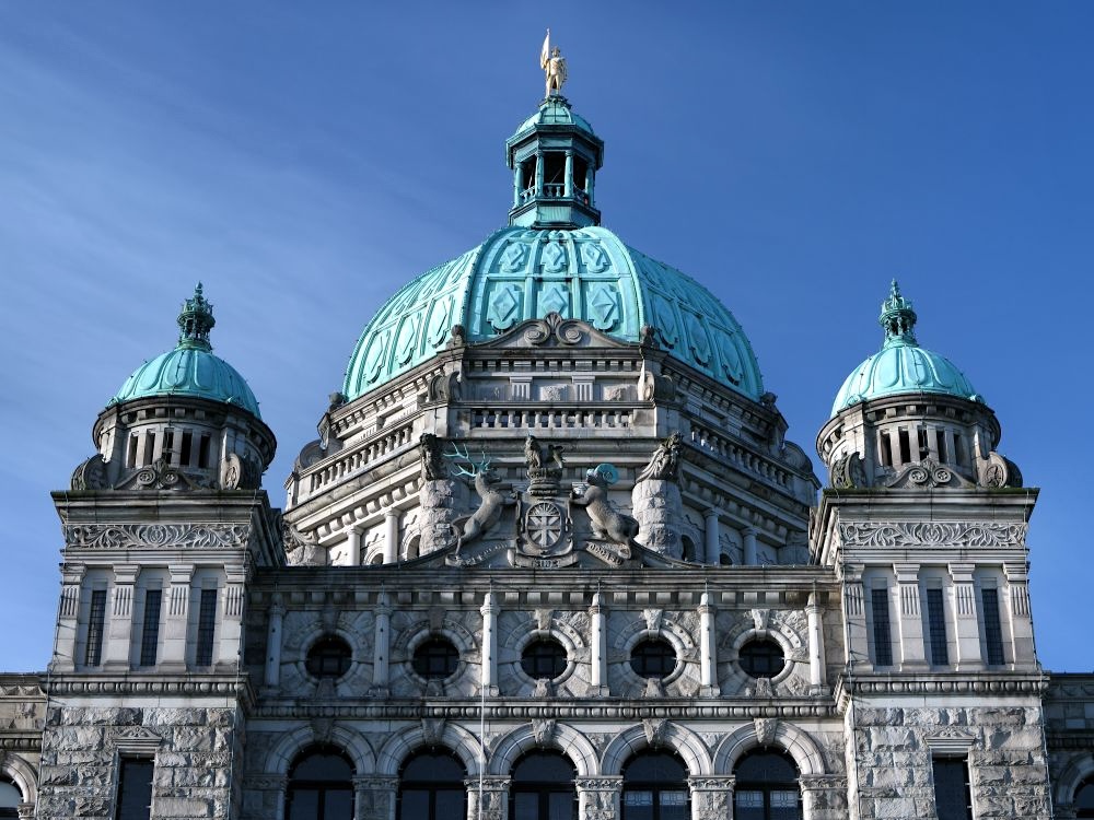 The upper facade and dome of the B.C. legislature, against a blue sky.