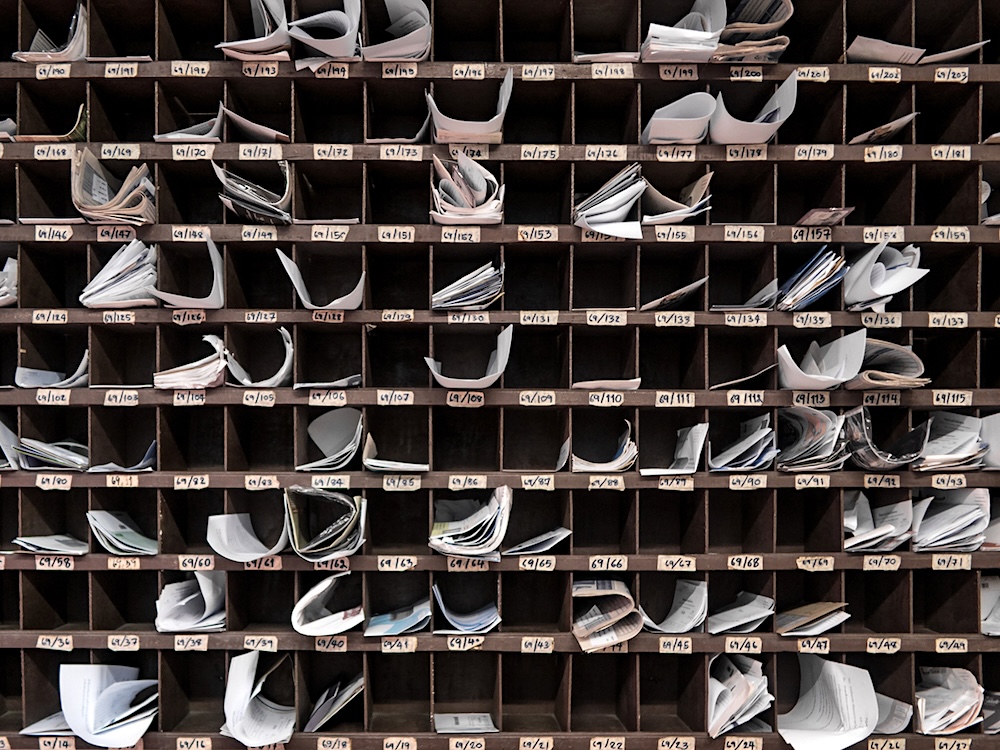 In an apartment mail room, mail cubbies are stuffed with letters.