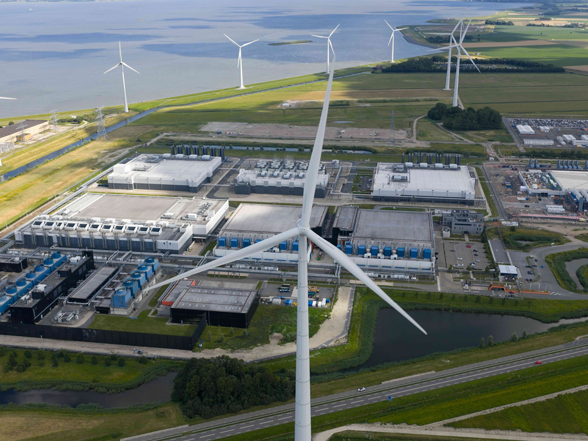 An aerial view shows a sprawling complex of buildings on the edge of the sea, with eight large windmills.