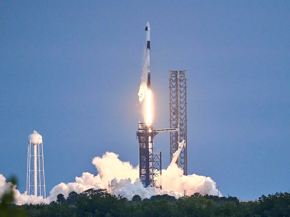 A white and black rocket blasts off under a deep blue sky.