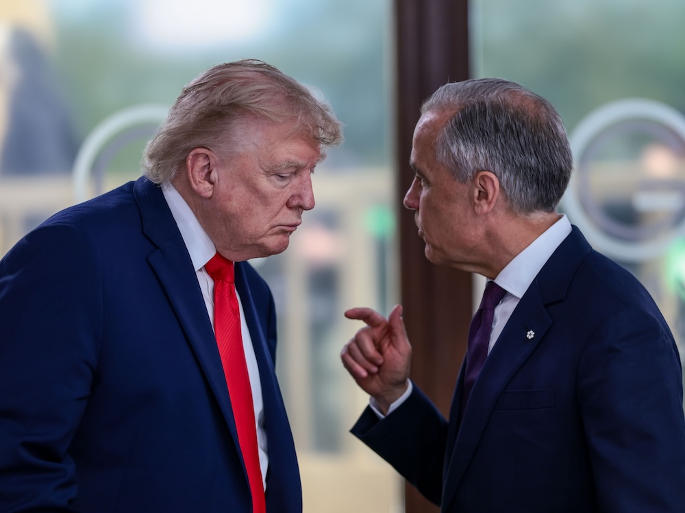 Donald Trump and Mark Carney stand very close together, with Carney gesturing to make a point.