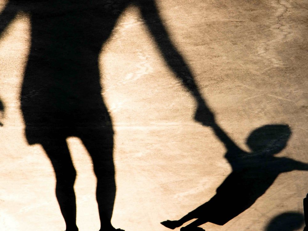 A shadow of a woman holding the hand of a young child against a concrete surface in golden light.