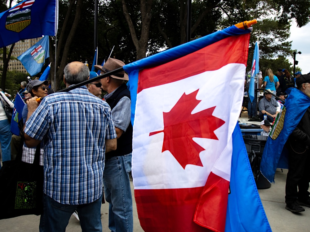 A man holds a flagpole with a Canada flag and an Alberta flag.