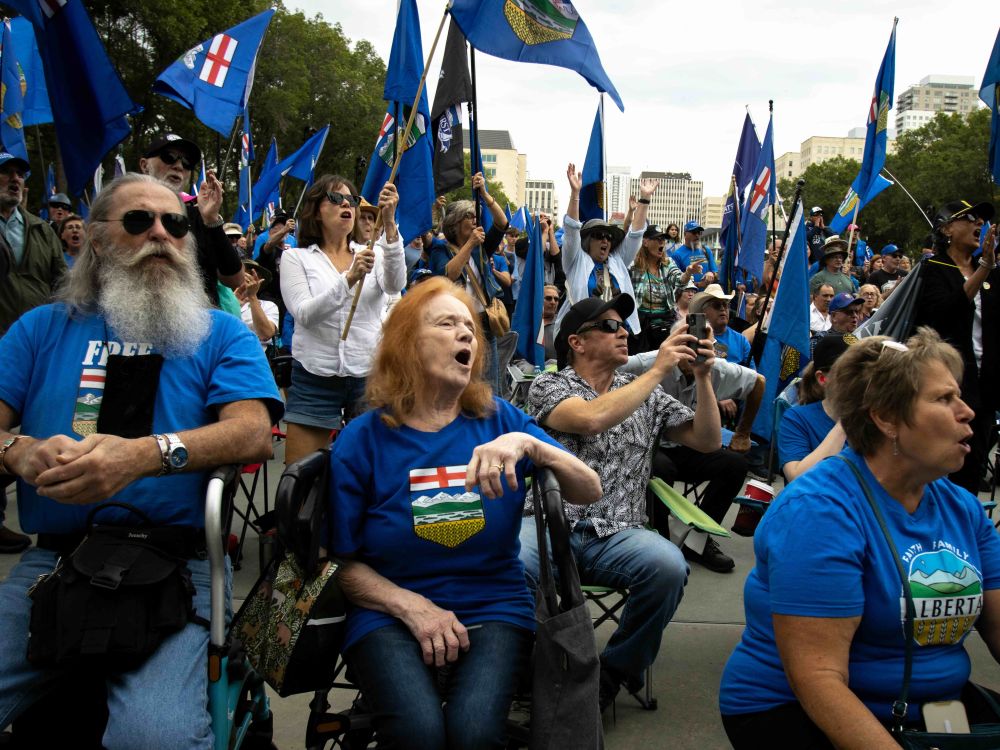 A large crowd in blue T-shirts, some waving flags, are on a plaza.