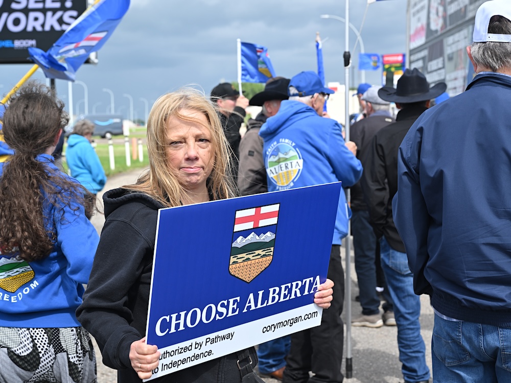 A woman with blond hair holds a blue sign that says &lsquo;Choose Alberta.&rsquo;