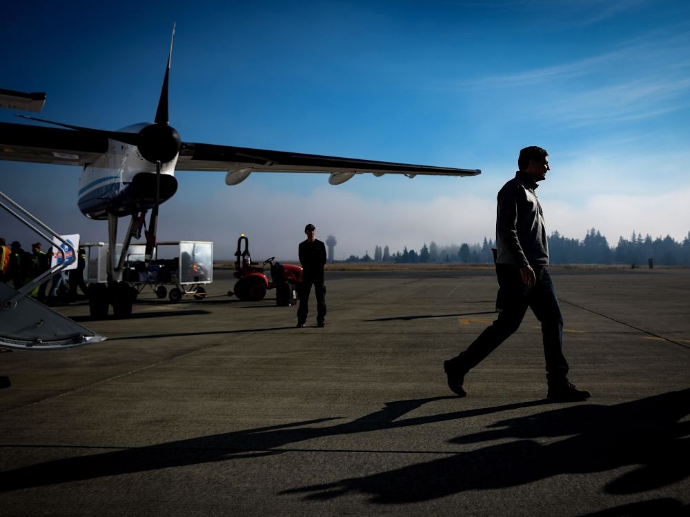David Eby walks across the tarmac after exiting a plane. The sky is blue and long shadows are seen on the ground.