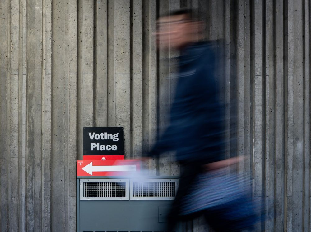 A blurred male walks by a sign with an arrow and the words &lsquo;voting place.&rsquo;