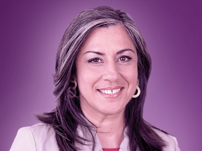 A profile photo in a purple hue of Maria Vassilakou from the shoulders up over a purple background.