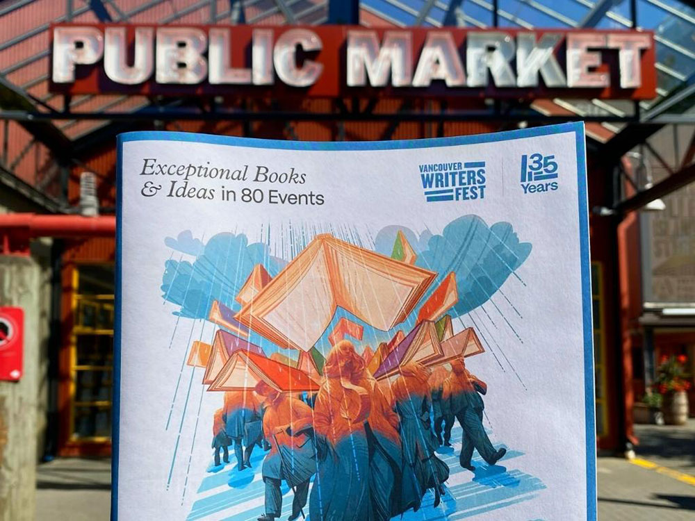 A program guide for the 2022 Vancouver Writers Fest is held up in front of the entrance to the Granville Island Public Market. The words ‘Public Market’ are visible in the background.