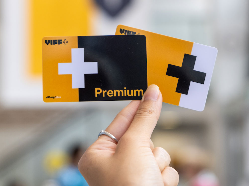 A person’s hand holds up two yellow and black cards that say “Premium” and “VIFF+.”