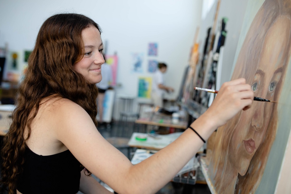 A young person paints a large, detailed, lifelike portrait.