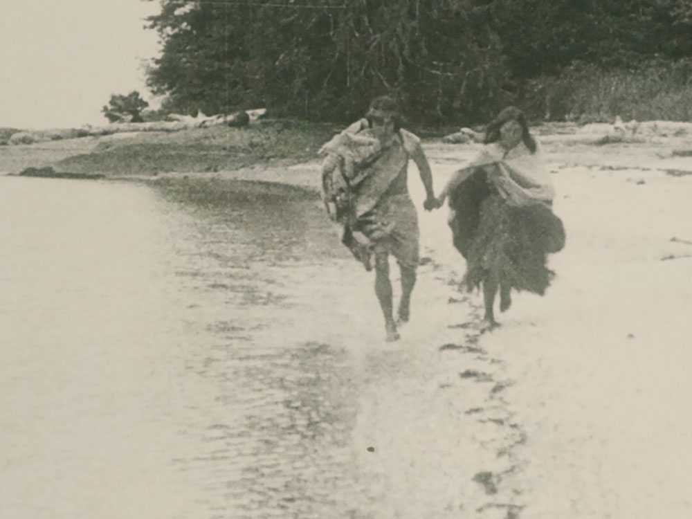 Two people holding hands skip along a beach in a faded, sepia-tone, century old photograph.
