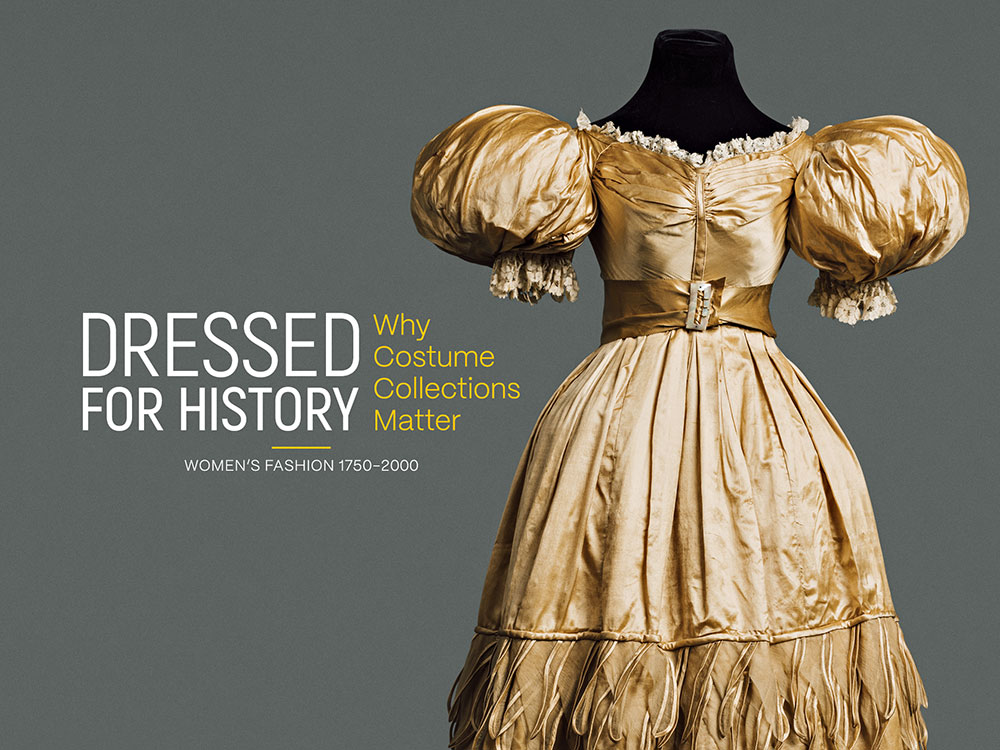 A gold evening dress with large puffy sleeves, circa 1830-35. Sans-serif text reading ‘Dressed for History’ floats to the left of the dress.