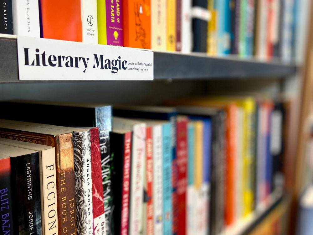 A line of bookshelves with a sign that reads ‘Literary magic.’