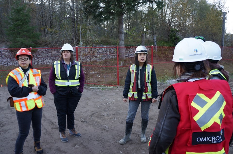 A group of women in hard hats and visi vests stand in a dirt area surrounded by a metal construction fence.