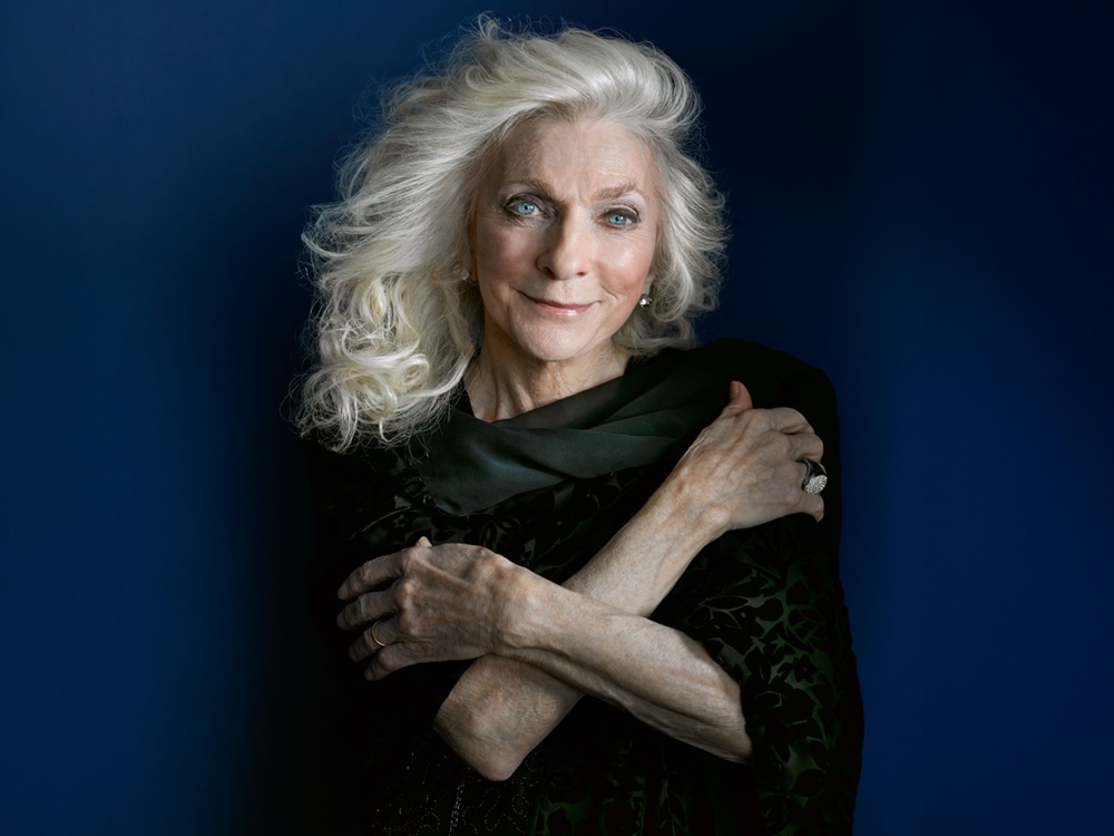 A woman in her 80s with light skin tone, blue eyes and silver-blond hair.