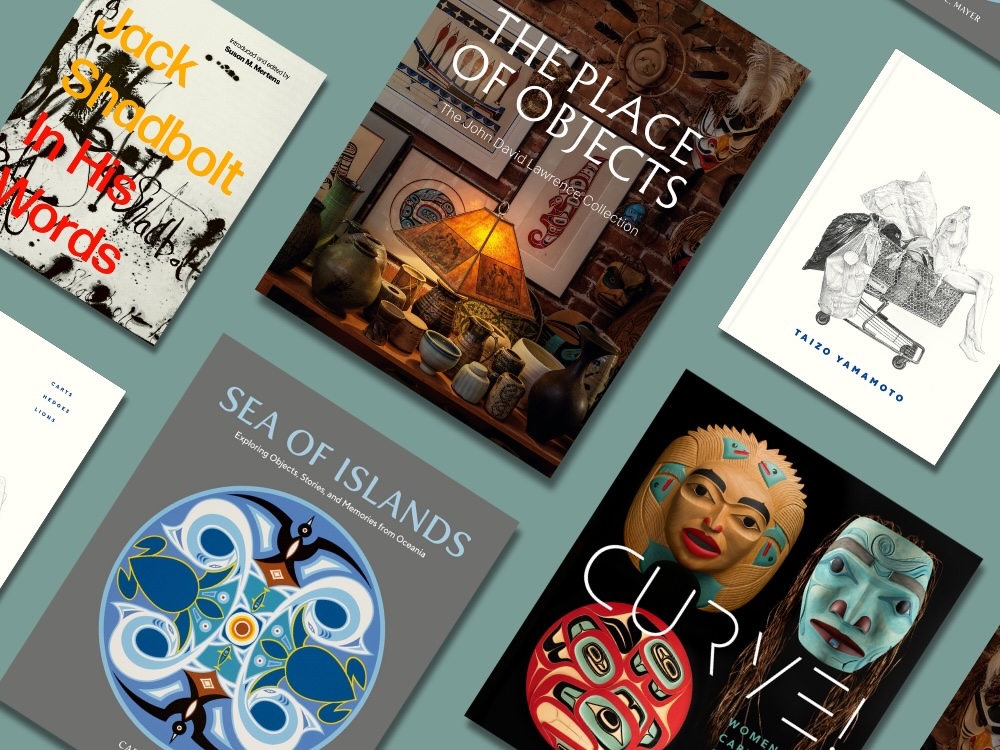 Five hardcover art books are arranged diagonally across the frame on a blue-green tabletop. Clockwise from left: ‘Jack Shadbolt: In His Words’; ‘The Place of Objects’; ‘Taizo Yamamoto: Carts, Hedges, Lions’; ‘Curve!’; ‘Sea of Islands.’