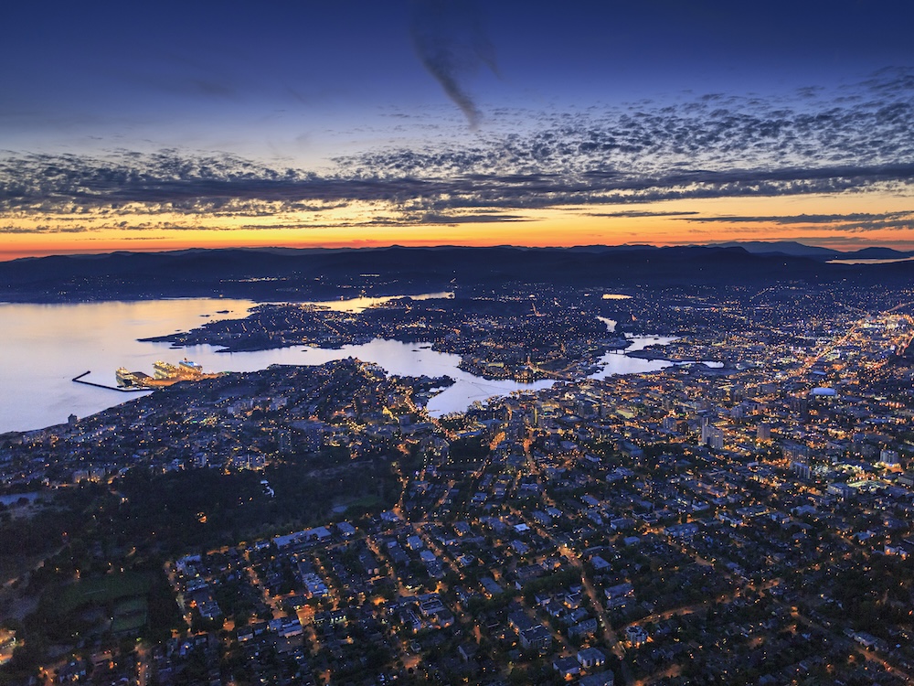 An aerial view of a lit-up waterfront city at dusk.