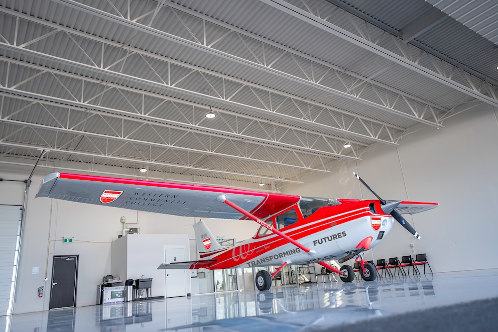 A small red and white airplane with the words &lsquo;Transforming Futures&rsquo; on its body sits inside a hangar.