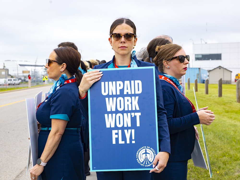WestJet employees stand together at an airport holding picket signs.