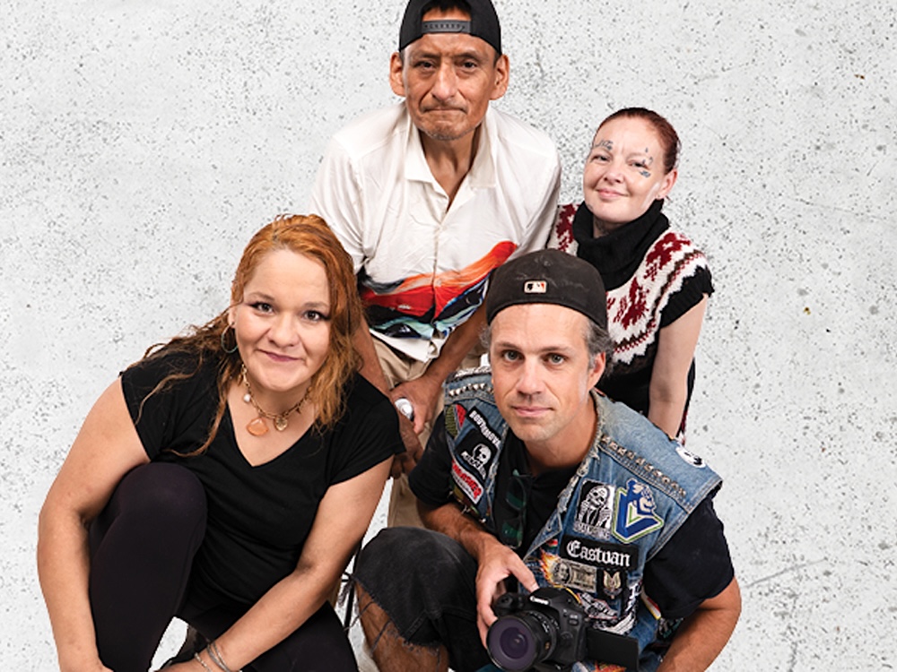 A group of four people looks upward toward the camera, crouching and smiling. 