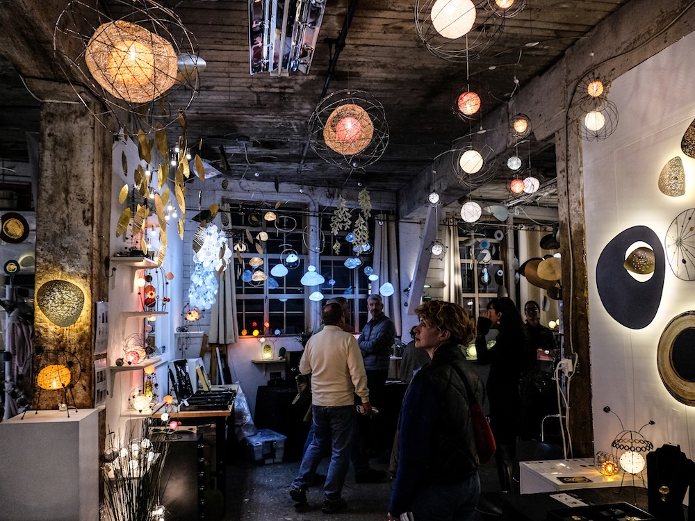 People wander through an artsy space filled with artistic lamps and other lighting fixtures.