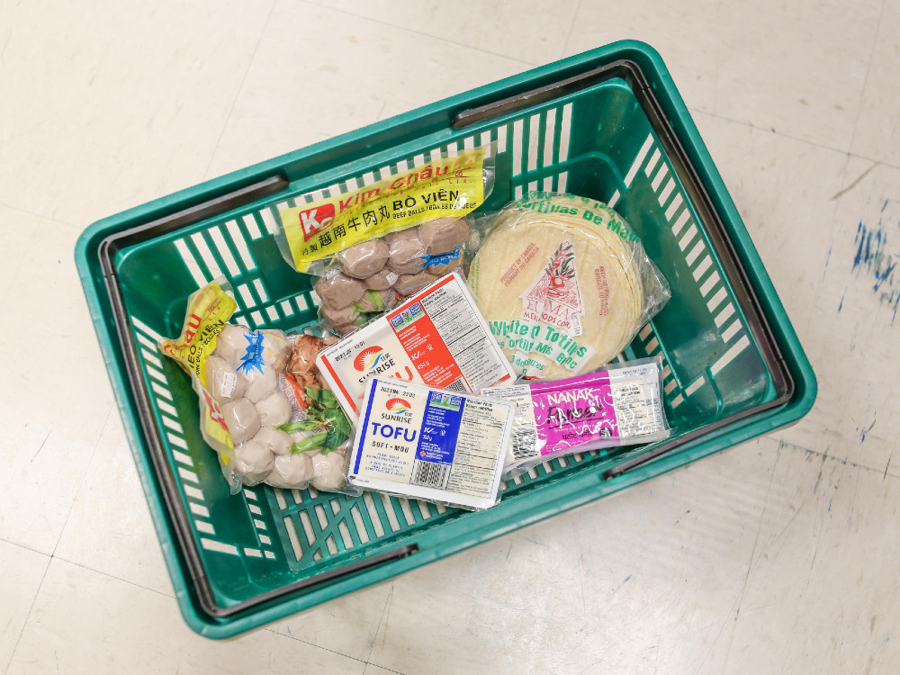 A green grocery basket with tofu, tortillas, paneer, beef balls and pork balls.