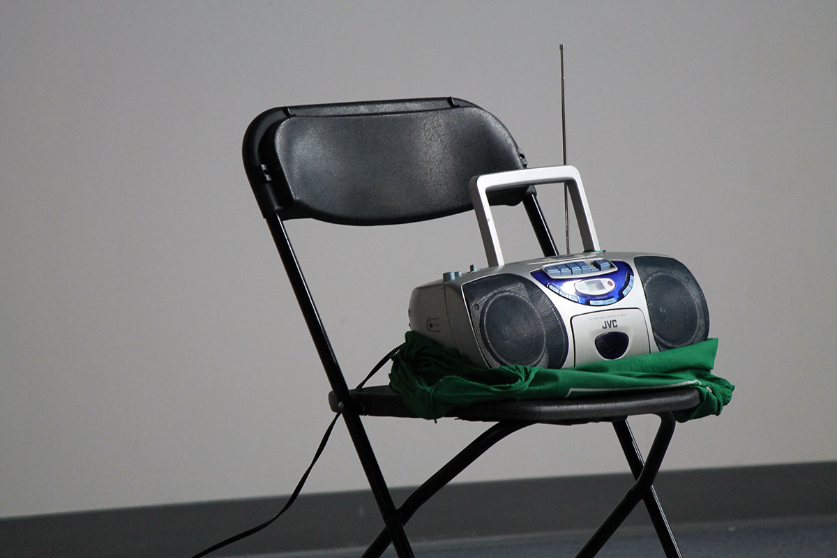 A boombox sitting on a folding chair plays music for a group exercise class.