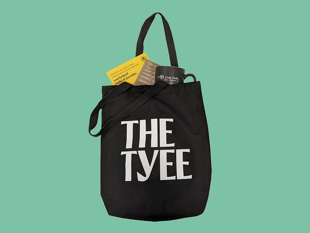 A black tote bag that reads ‘The Tyee’ is set against a teal background. It is filled with Tyee swag — a cup, notebook and notecard with pin.