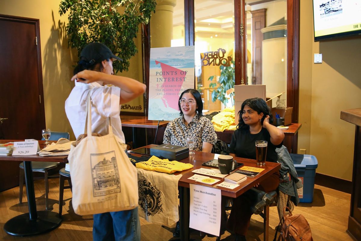 Tyee staffers at a merchandise table, with a large poster of the 'Points of Interest' cover behind them.