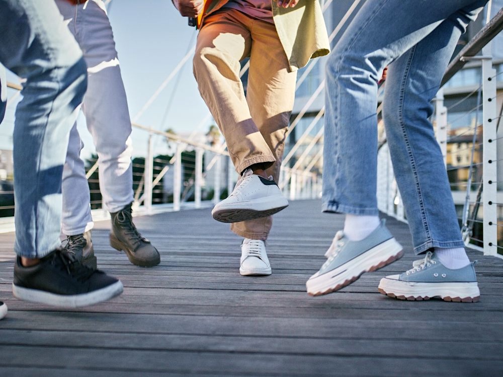 The legs of four people dancing on an urban footbridge.