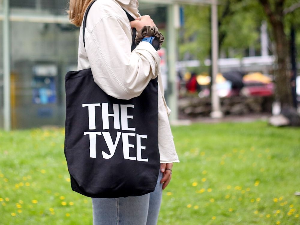 A close-up of a person&rsquo;s torso standing in a park with a black tote that reads 'The Tyee' on their shoulder.