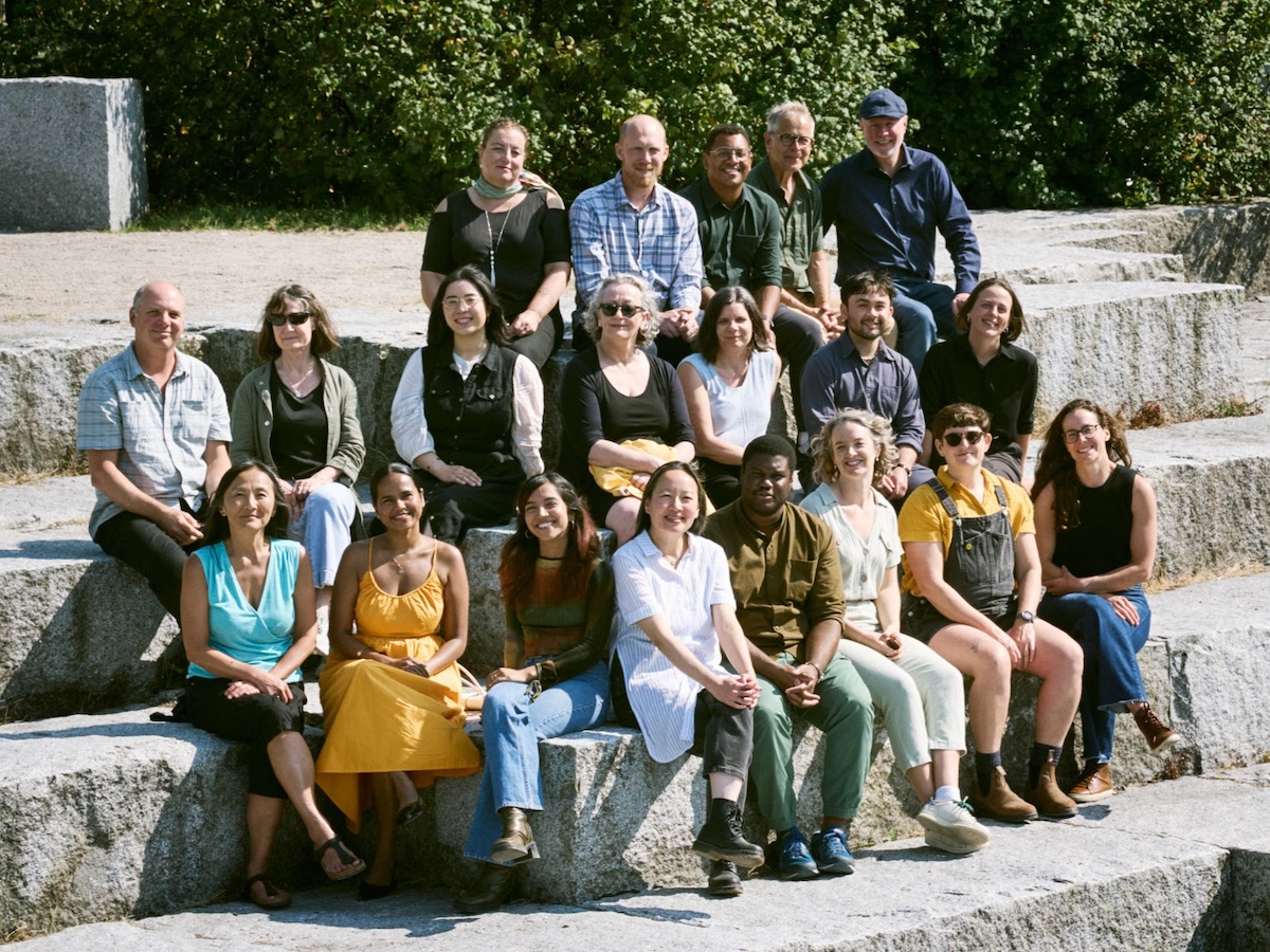 A group photo of Tyee staff seated on a set of thick grey concrete steps in the sun.