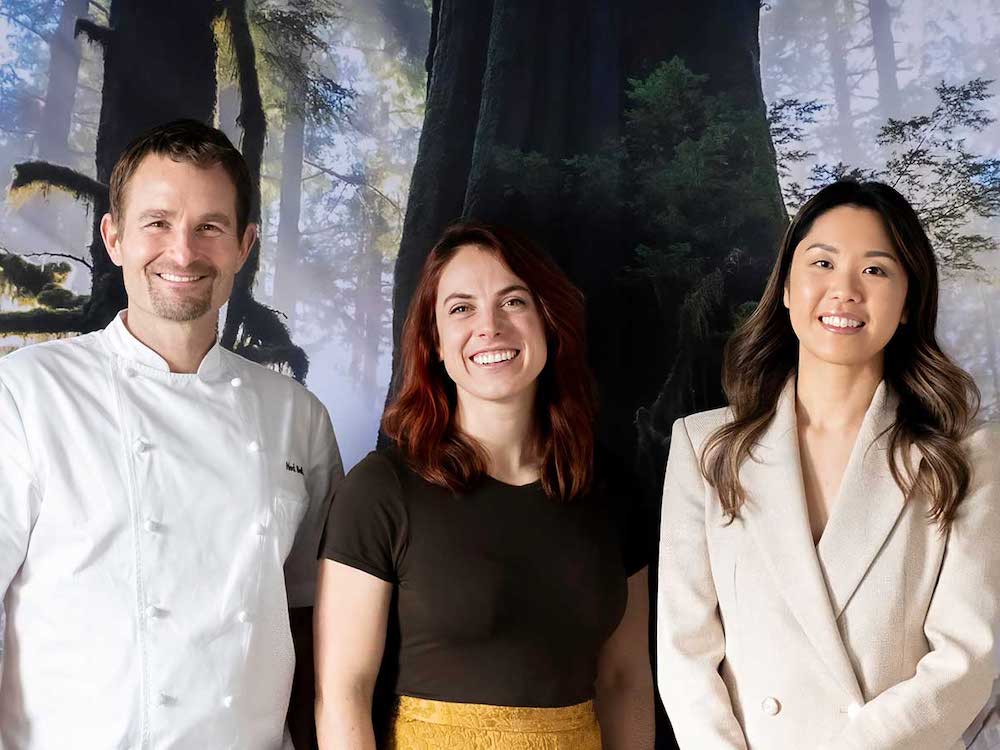 From left: a man with light skin and short brown hair wearing a white chef’s jacket; a woman with light skin and medium-long reddish-brown hair wearing a black shirt; and a woman with medium-light skin with long black hair wearing a linen-coloured blazer.