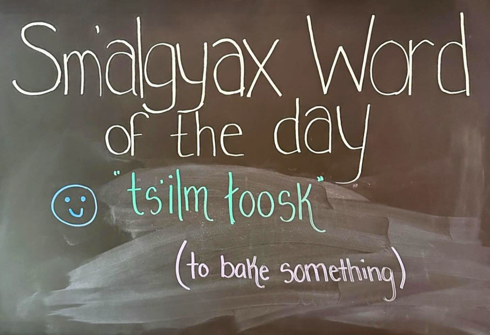 An image of a chalk board with the words “Sm’algyx word of the day: ts’ilm toosk, to bake something.”