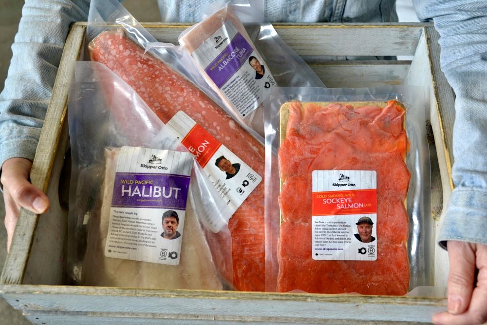 A wooden crate contains packaged seafood such as halibut, tuna and salmon. Each product label bears a photo of the fisher who caught the fish.