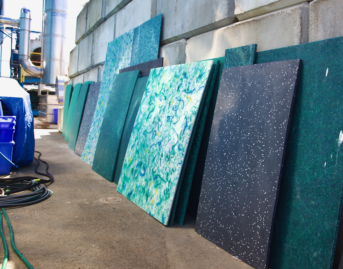 Squares and rectangles of plastic board in blue, white, green and black, embedded with colourful pieces of rope, lean against a concrete block wall.