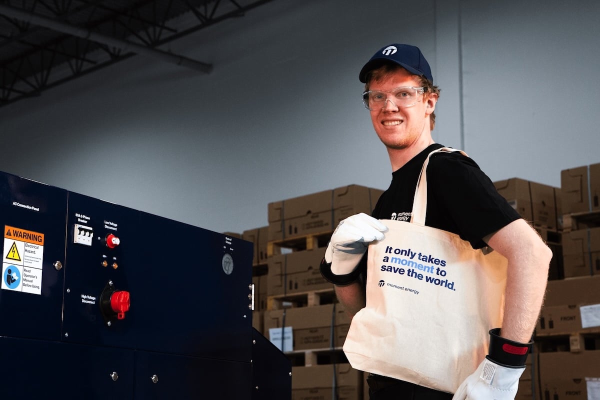A staff member at Moment Energy inside a warehouse holds a tote bag. It reads, ‘It only takes a moment to save the world.’