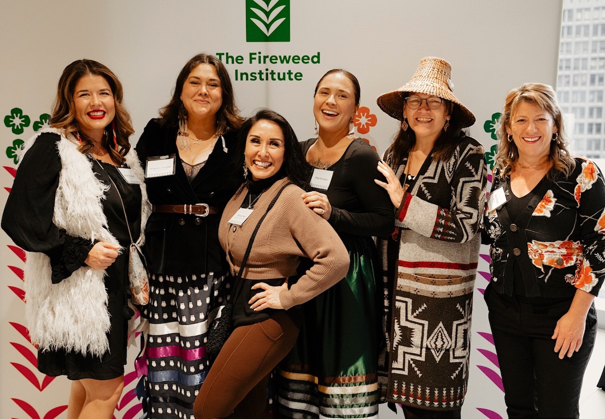 A group of women stand in front of a sign with the words ‘Fireweed Institute’ written on it.