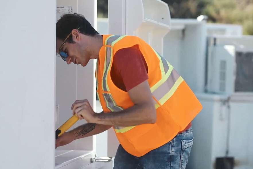 A man in a high-visibility vest and red T-shirt tries to pry pieces of plastic from inside a refrigerator.
