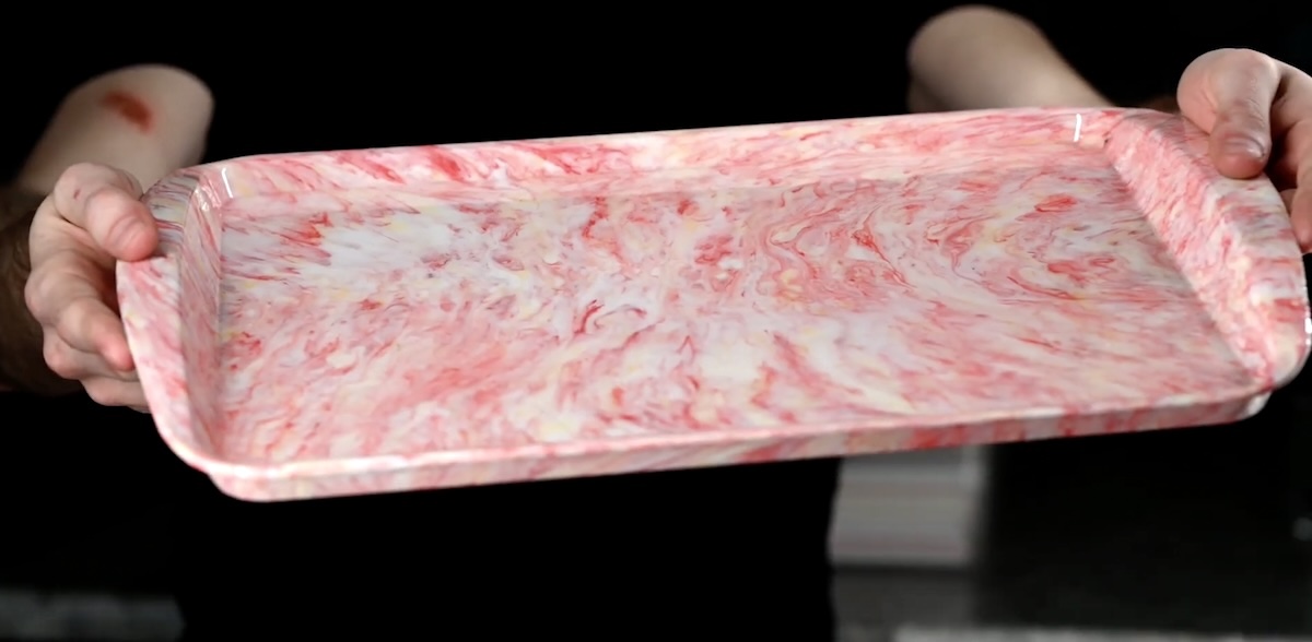 A man holds a red and white tray made of disposable straws.