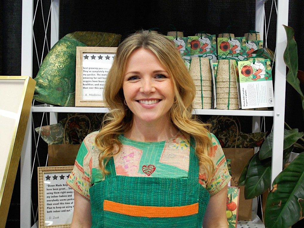 A woman with light skin and long blond hair smiles at the camera.