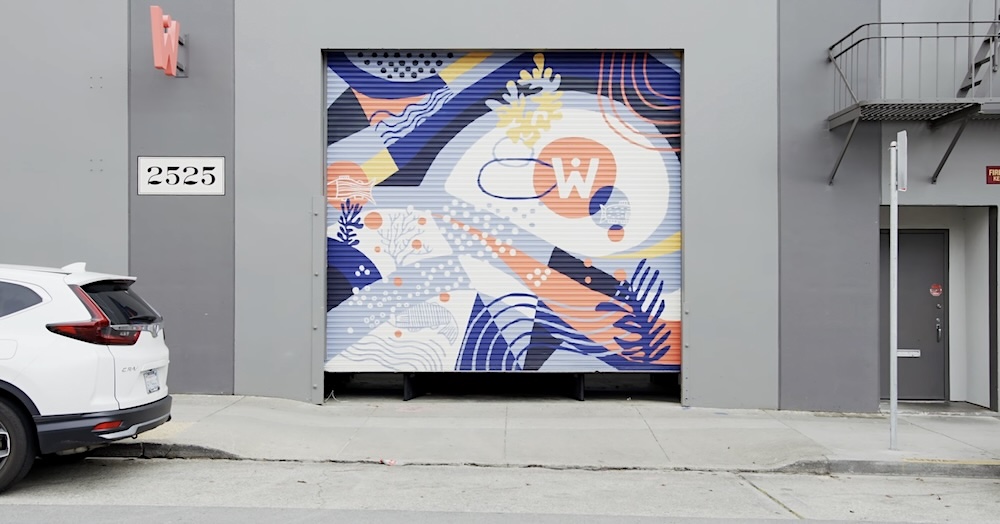 A multicoloured sliding door with a large &lsquo;W&rsquo; slides open. A white Honda CRV is parked on the street. 