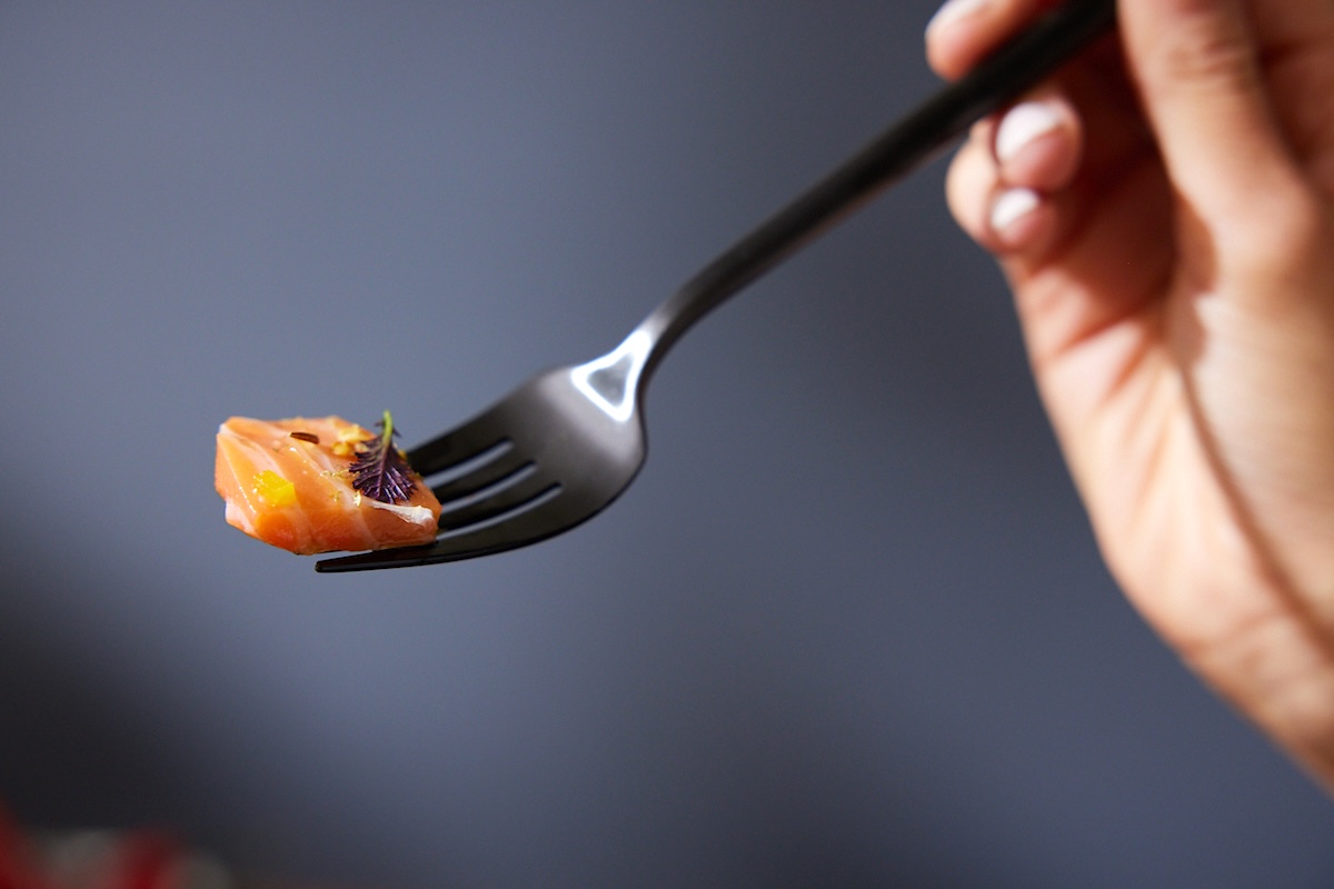 A piece of cultivated salmon on a fork. There&rsquo;s a tiny leaf and some dressing on the meat. 
