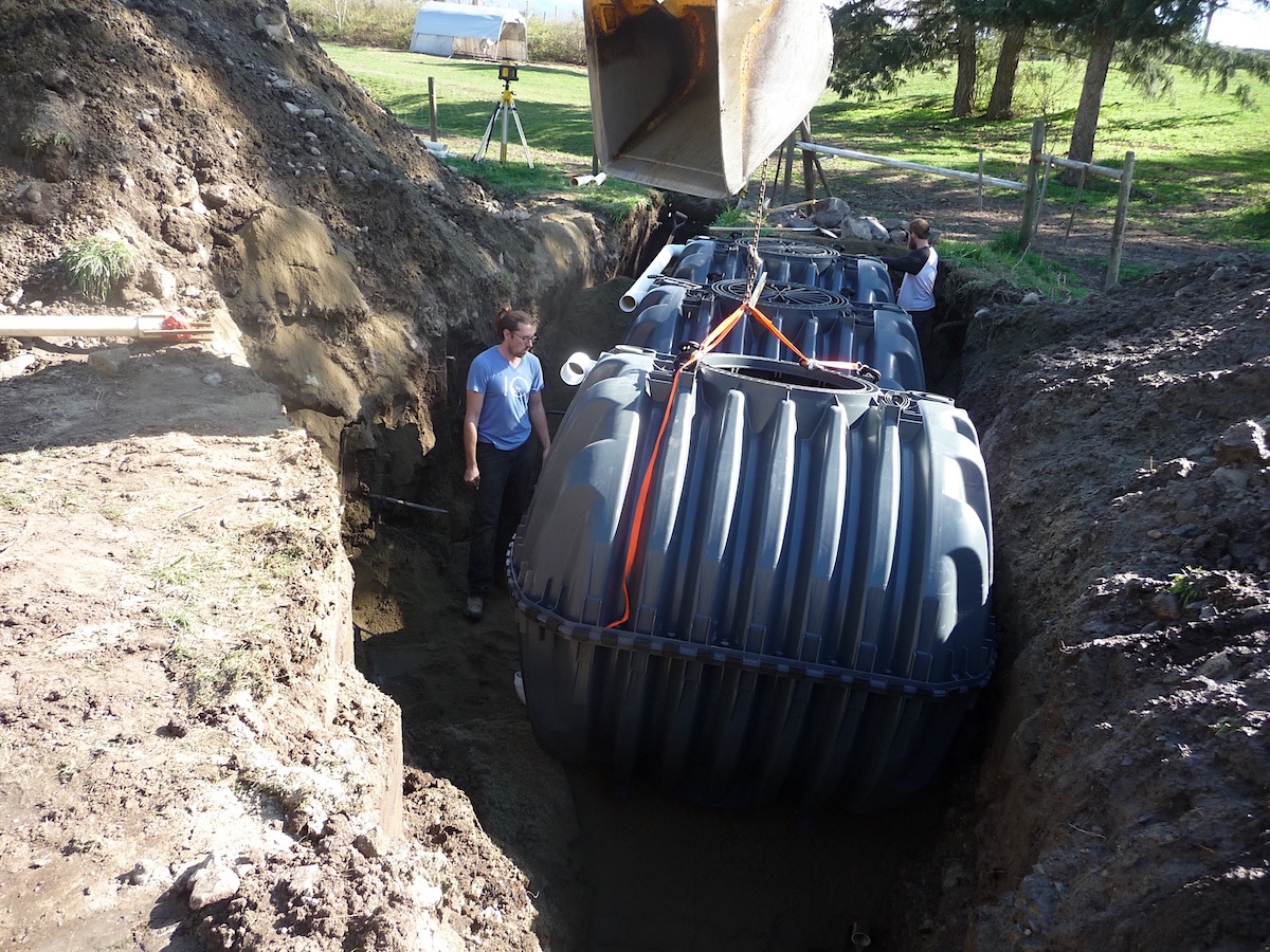 Men work in a pit to position three large plastic water tanks. 